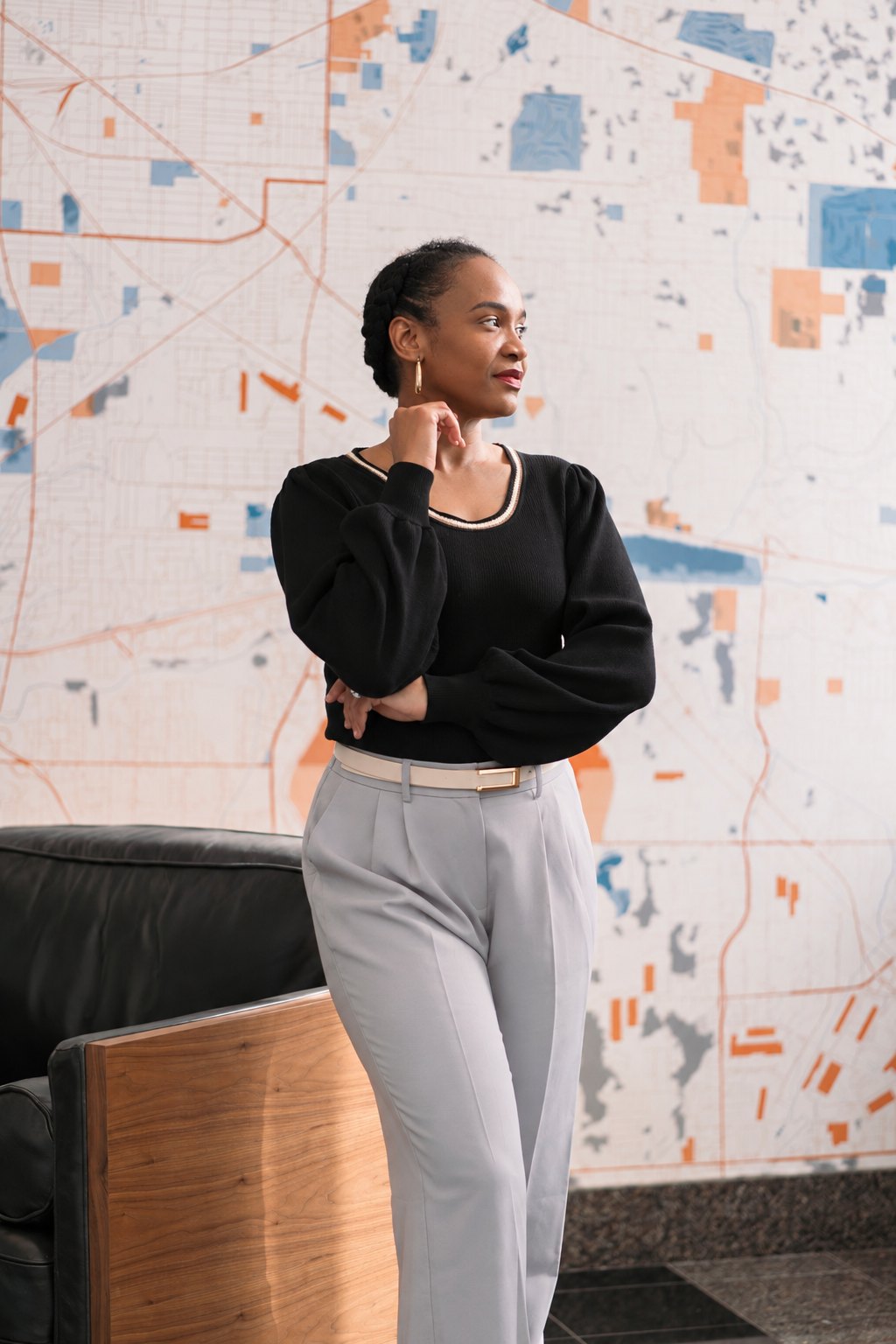 Chief Nnakina Xi-Amaru Fears, business educator and speaker, in a black sweater and grey trousers in front of a city map mural